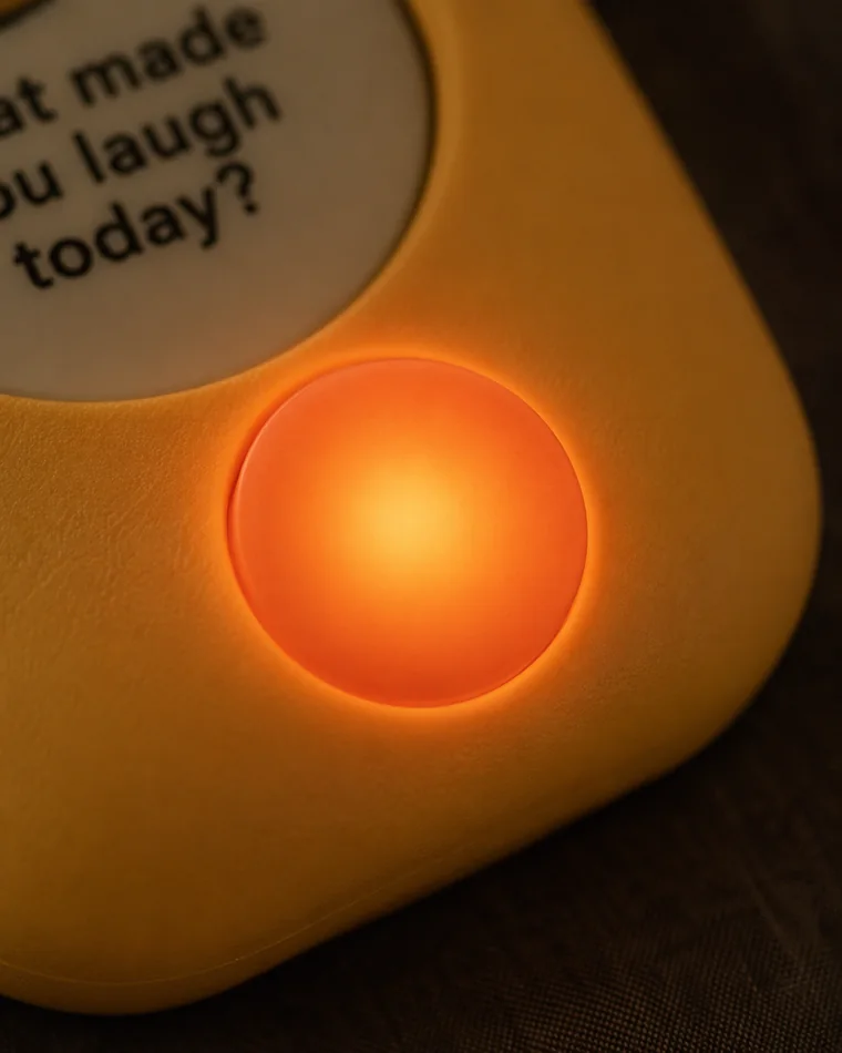 The Warm device's coral button glowing warm amber at dusk, the once-a-day reminder that it's time to talk